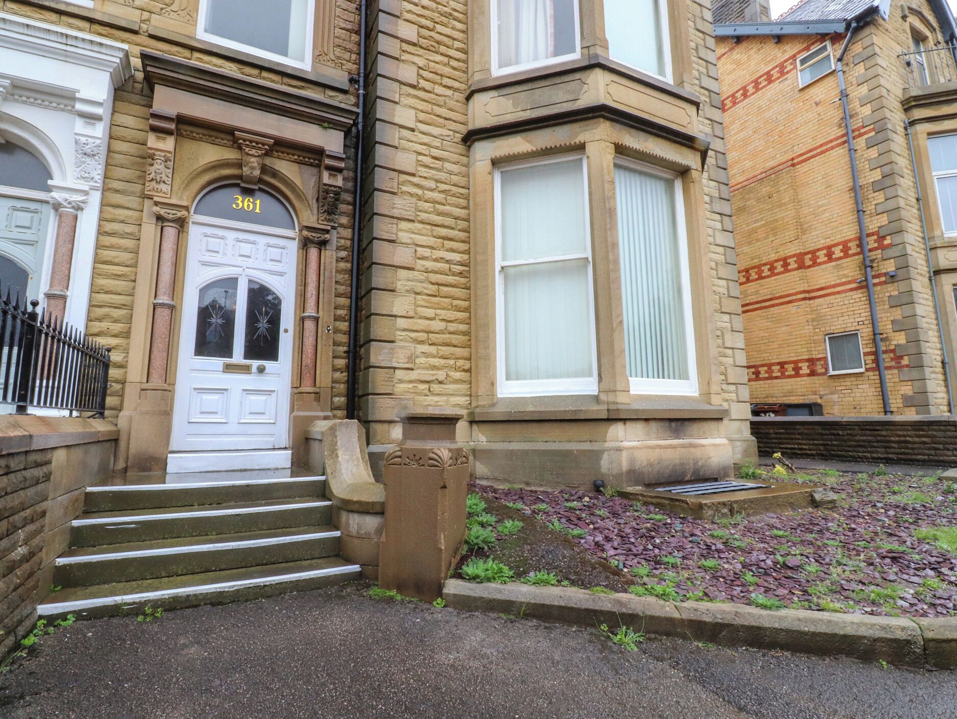 A traditional two-story building with a white front door, numbered 361, and a small garden area with stepping stones.