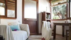 Ein Zimmer mit einem Bett, einer Holztür, einem Fenster mit Blick auf Bäume, einem Tisch mit einer Vase und einem Stuhl.