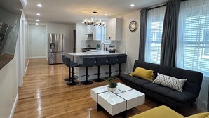 A modern living room with a sofa, coffee table, and a kitchen area in the background. - Modern Brand New Dorchester Apartment! Quiet, Convenient & Minutes from Boston! (Dorchester)