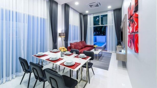 Una habitación de hotel moderna con zona de comedor, un sofá rojo y un ventanal con cortinas.