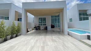 Un patio moderno al aire libre con piscina, plantas en macetas y una zona de estar cubierta.