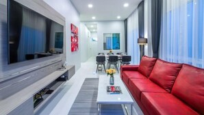Una sala moderna con un televisor de pantalla plana grande, un sofá de cuero rojo, un comedor con mesa y sillas, y una cocina al fondo.