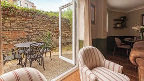 Una habitación acogedora con pared de piedra, zona de comedor con sillas metálicas y una mesa, y un sillón a rayas.