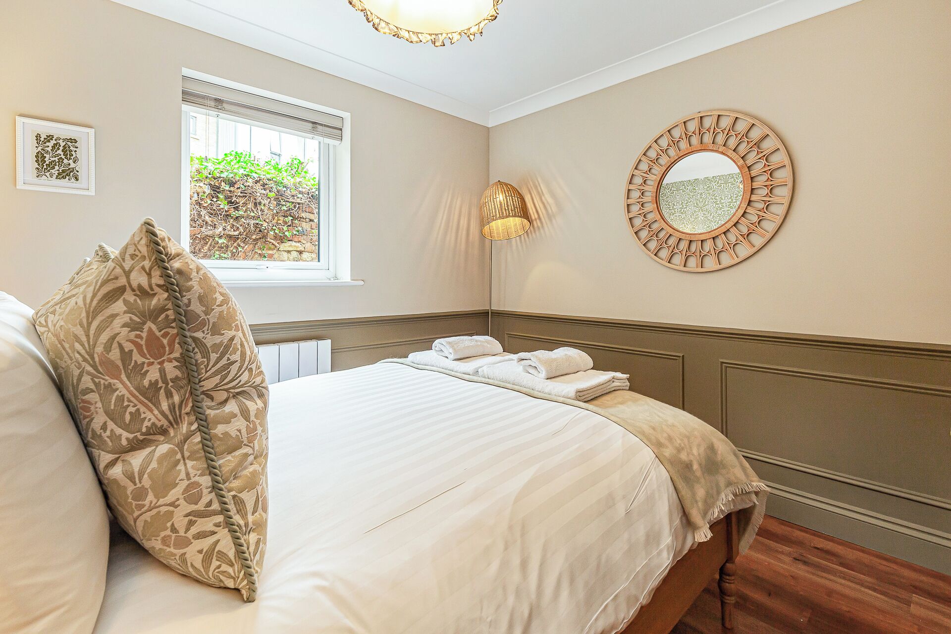 A neatly made bed with a floral pillow, a bedside lamp, and a round mirror on the wall.