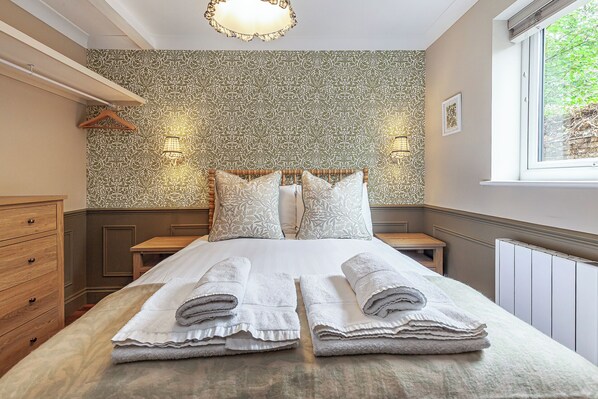 Een keurig opgemaakt bed met gerolde handdoeken, een houten hoofdbord en behang met een patroon.