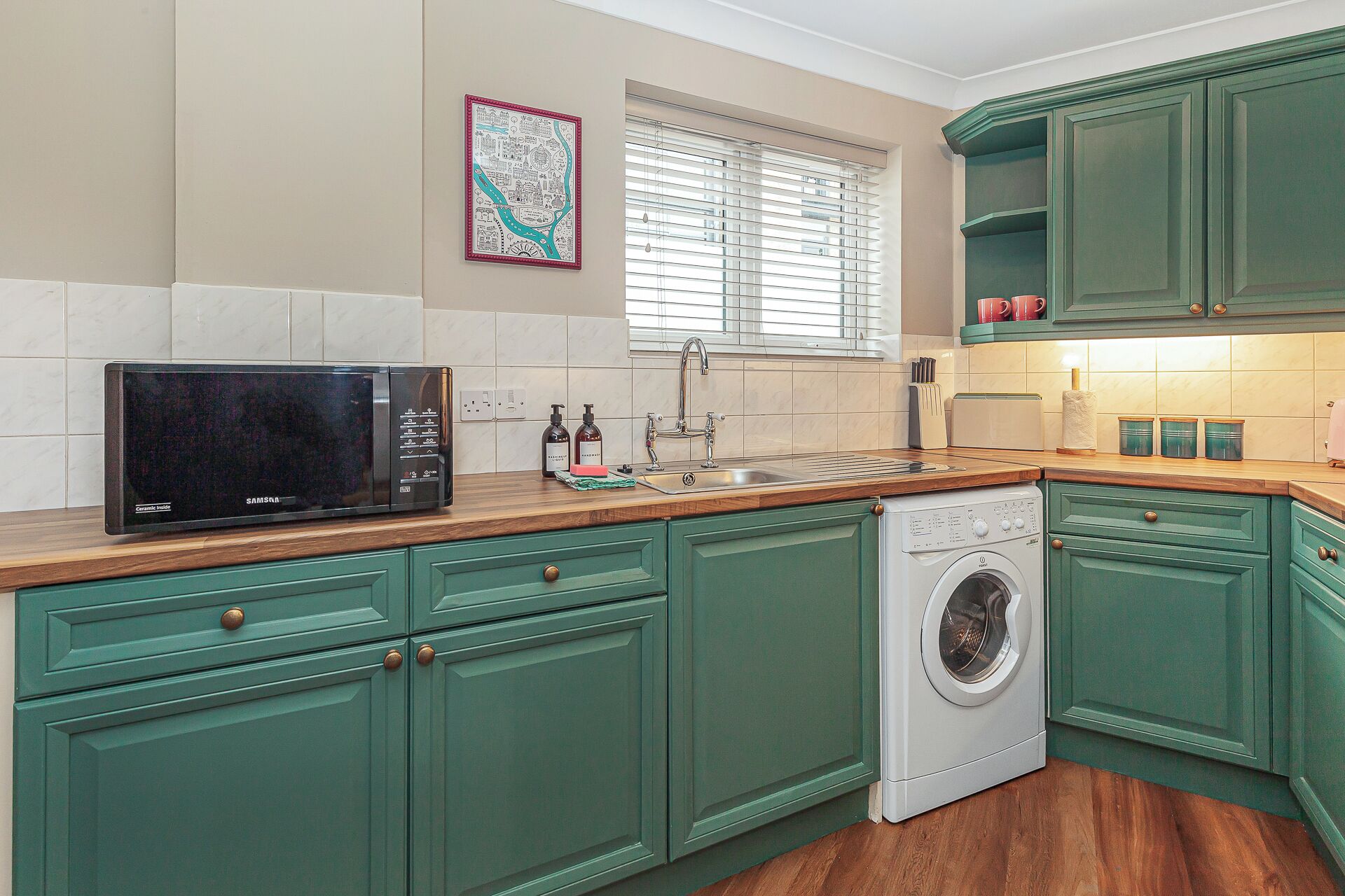 A kitchen with green cabinets, a microwave, a sink, and a washing machine.