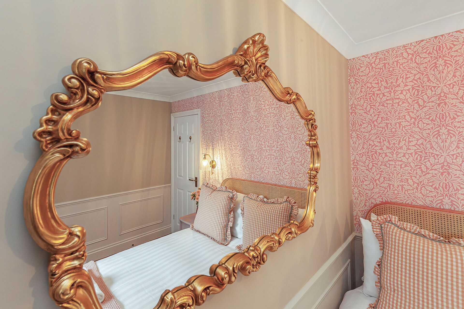 A bedroom with a large ornate mirror, a bed with checkered bedding, and a door leading to another room.