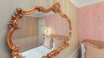 A bedroom with a large ornate mirror, a bed with checkered bedding, and a door leading to another room.