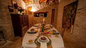 A long dining table set with plates, glasses, and a candle, in a room with stone walls and wooden furniture. - Atlantis 12 Maison d’hôtes et d’art (Ounagha)
