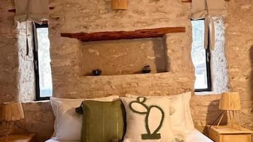 A rustic bedroom with a stone wall, wooden beams, a bed with green bedding, and two bedside lamps.