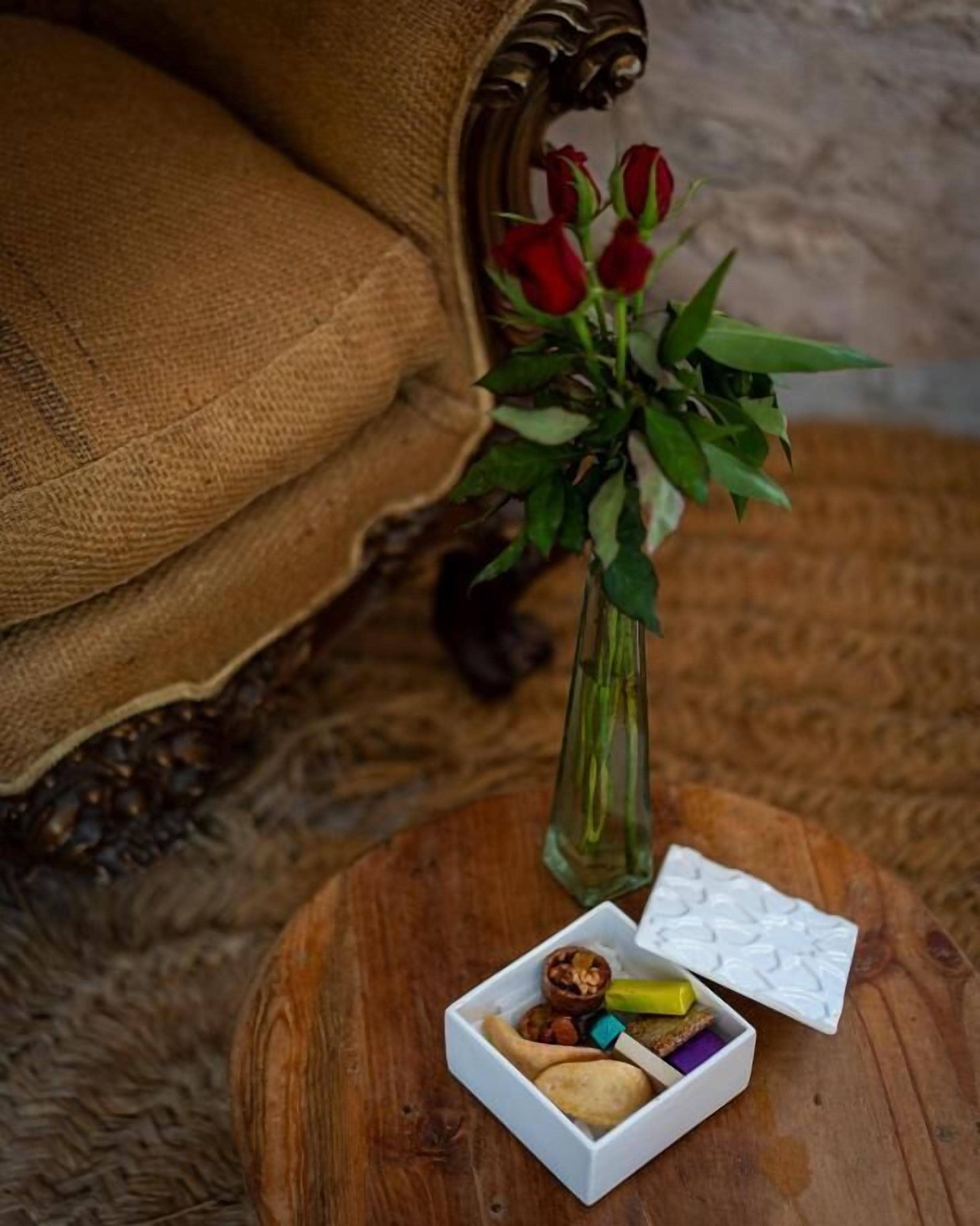 Una mesa de madera con un jarrón de rosas rojas, una caja pequeña de frutos secos y un adorno decorativo.