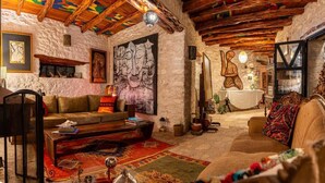 A cozy living room with a fireplace, rustic wooden beams, and a large abstract painting. - Atlantis 12 Maison d’hôtes et d’art (Ounagha)