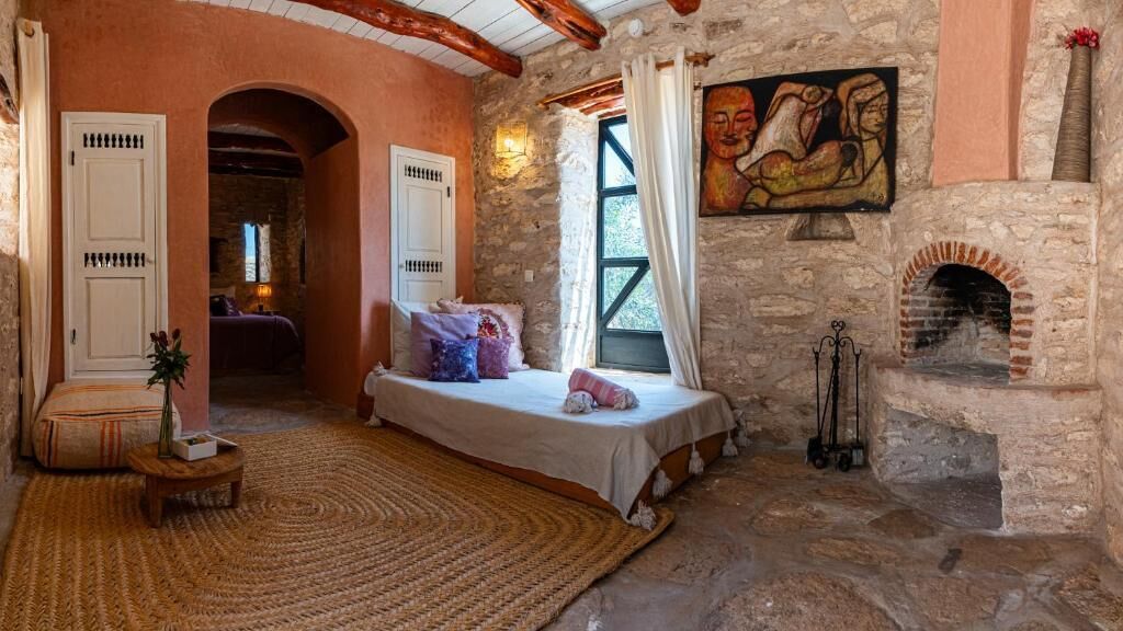 Una camera da letto rustica con un camino in pietra, un letto con cuscini e un quadro appeso al muro.