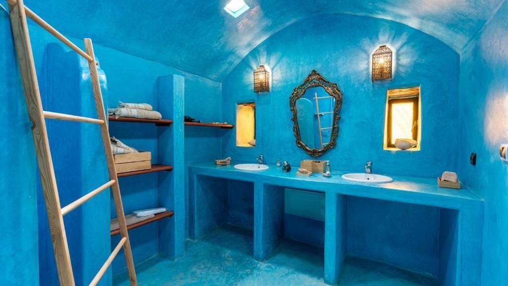 A bathroom with blue walls, a wooden ladder, and two sinks with mirrors.