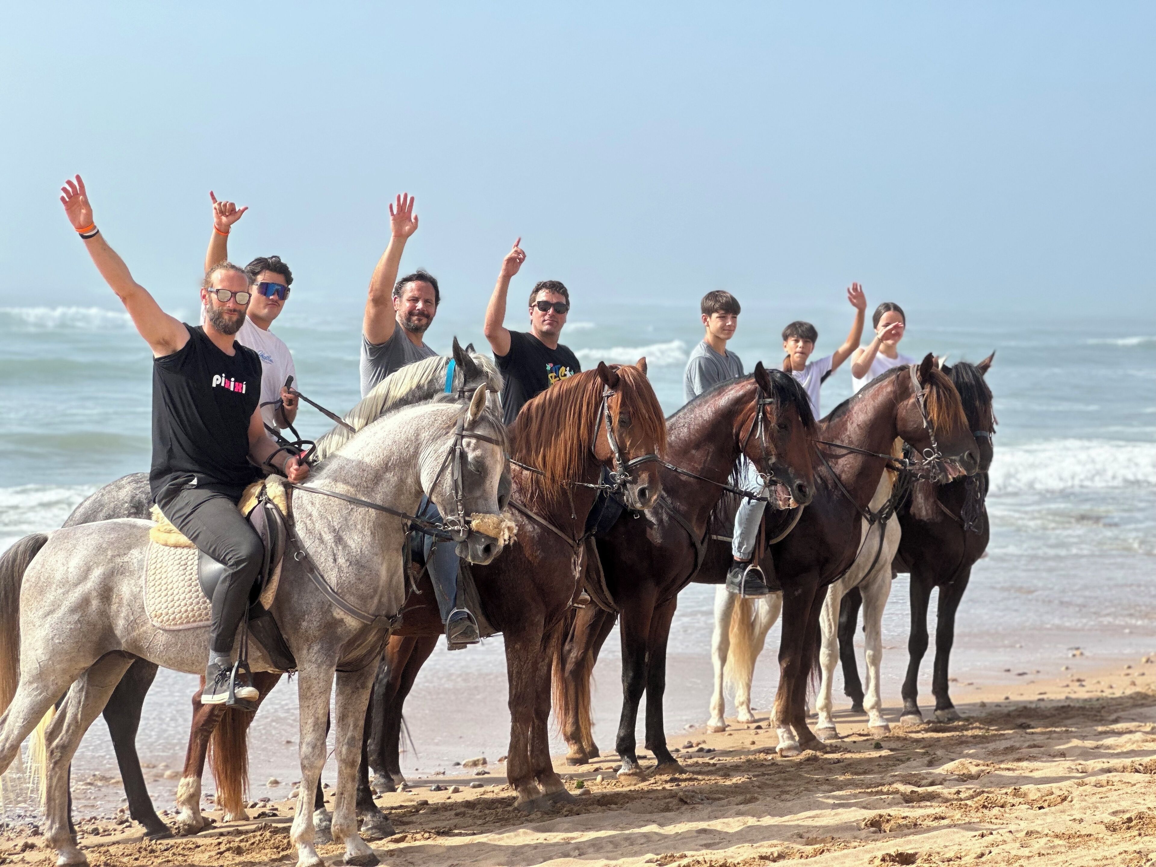 A group of people on horseback on a beach with the ocean in the background.