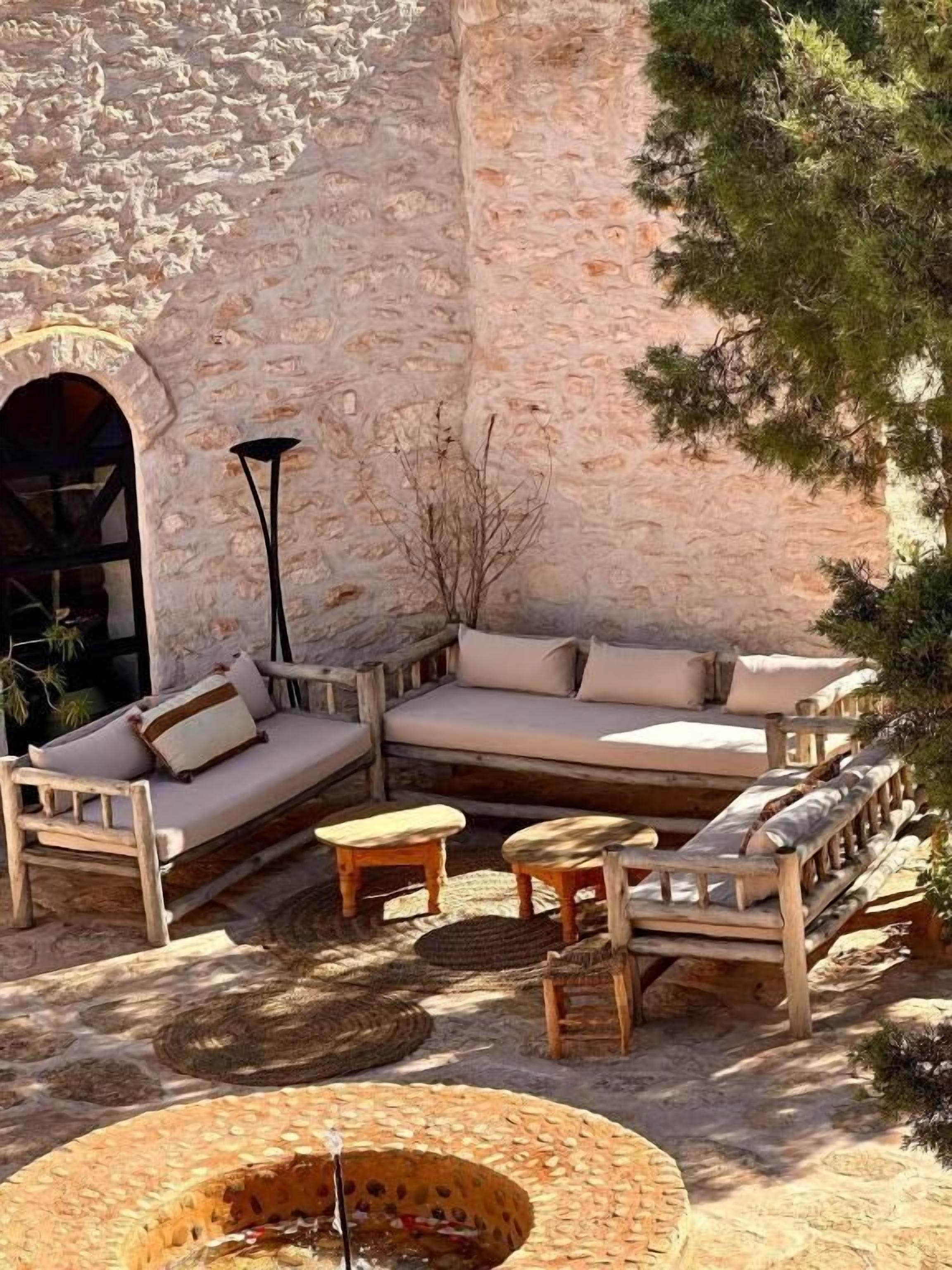 An outdoor seating area with a stone wall, wooden furniture, and a fire pit.