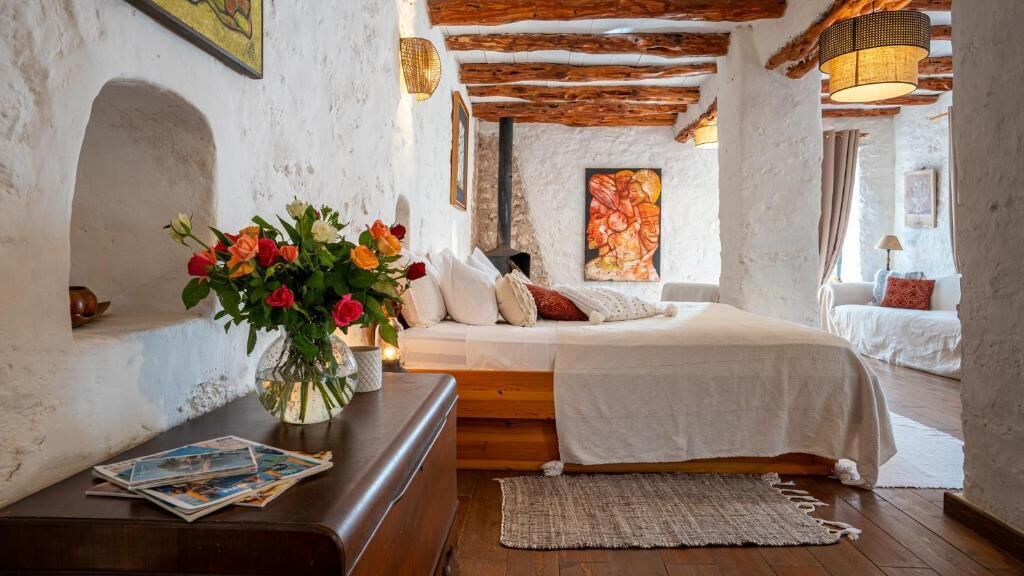 Une chambre confortable avec un lit en bois, un vase de fleurs et un mur en pierre rustique.