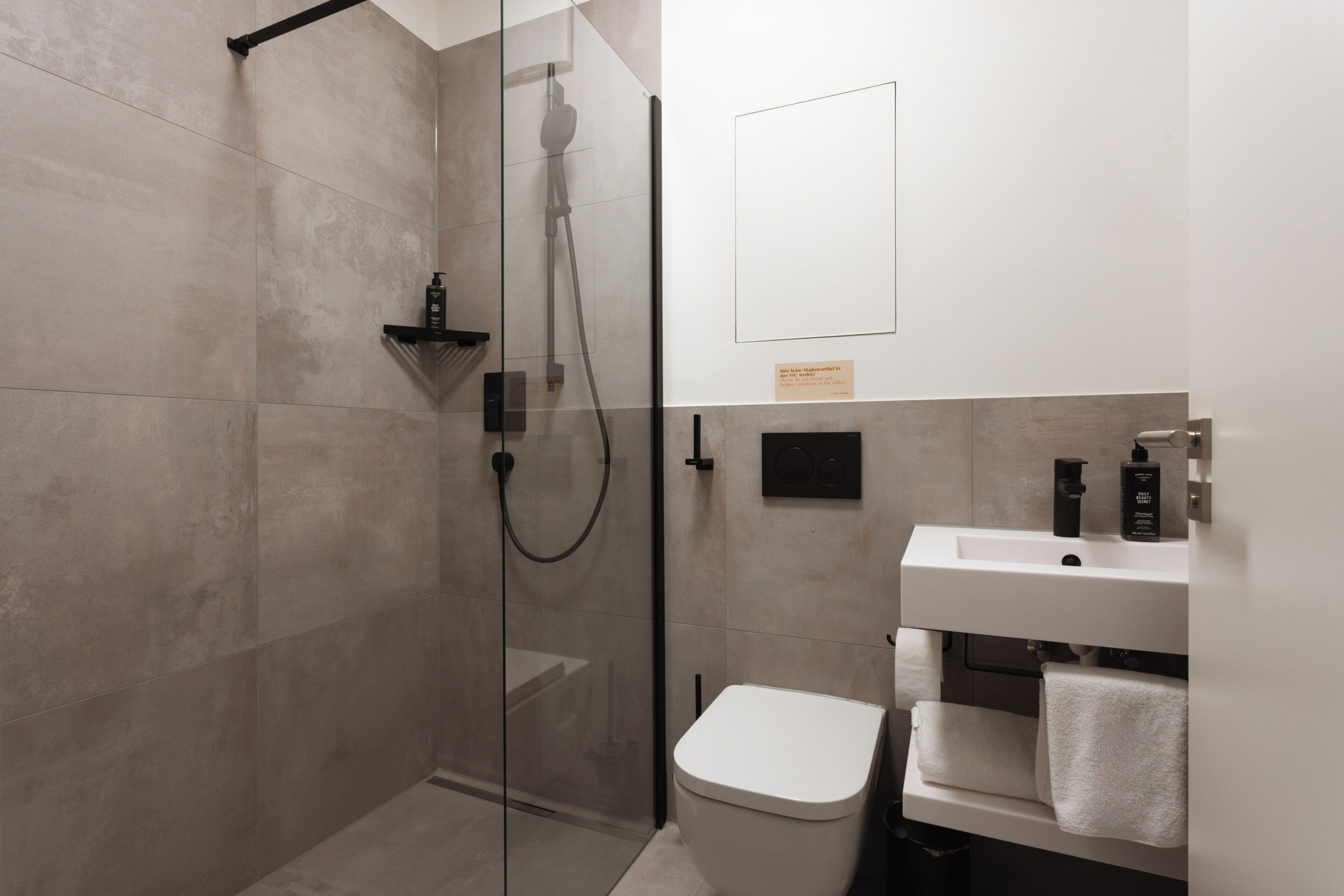 A modern bathroom with a glass-enclosed shower, a white toilet, and a sink with toiletries.