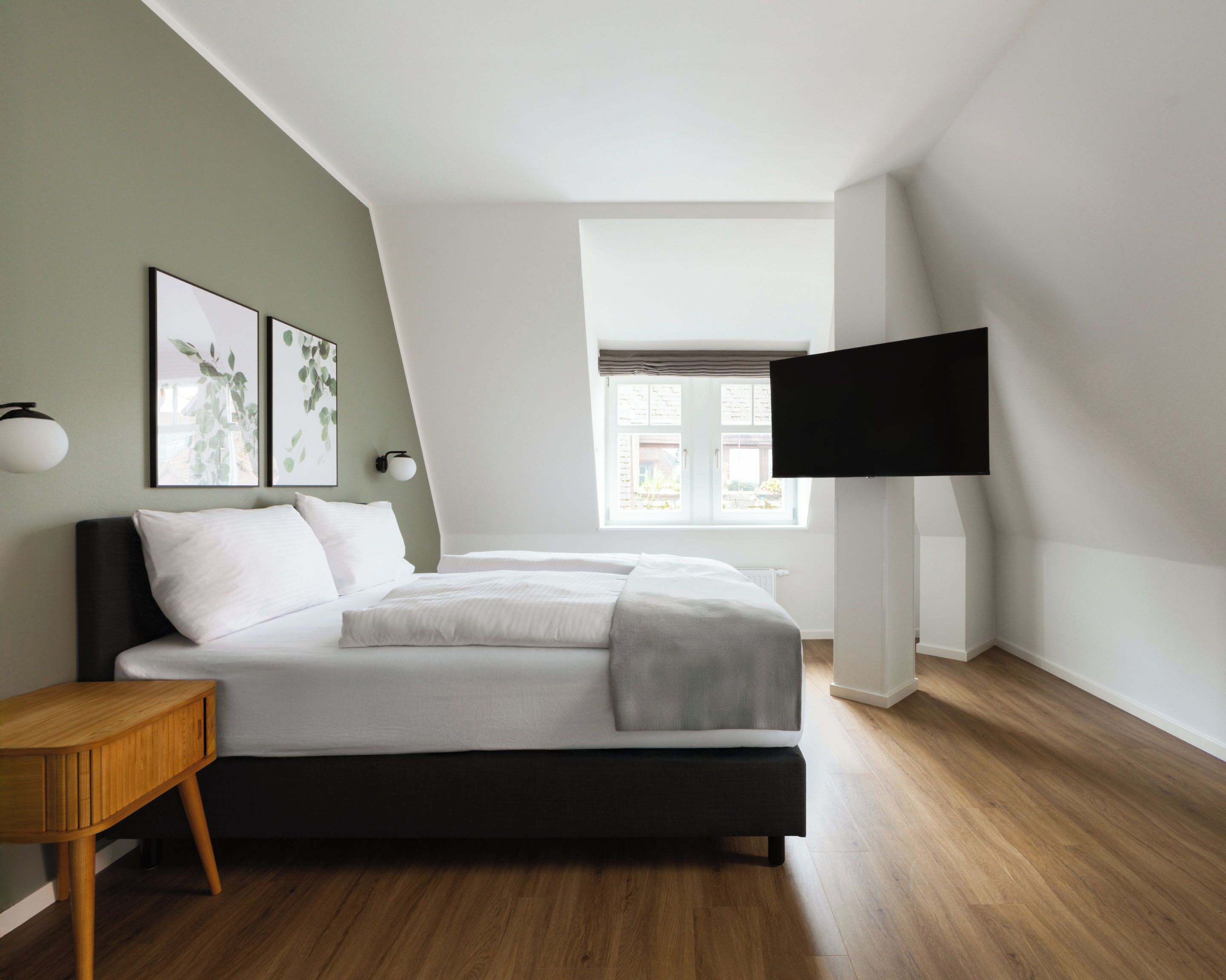 A modern bedroom with a bed, a TV mounted on the wall, and a window with a view.