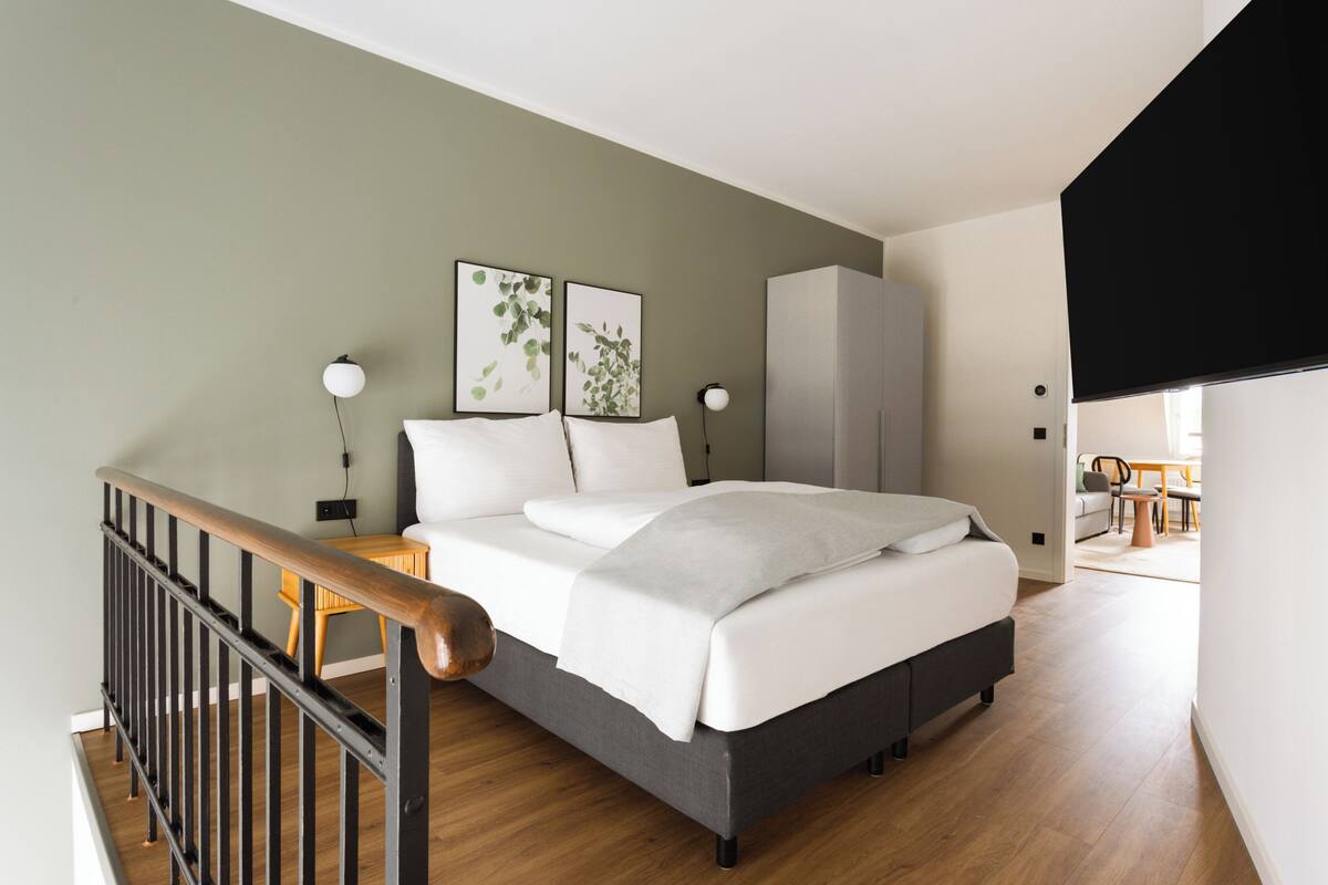 Una camera da letto moderna con un letto grande, una scala in legno, una televisione a schermo piatto e opere d'arte alle pareti.
