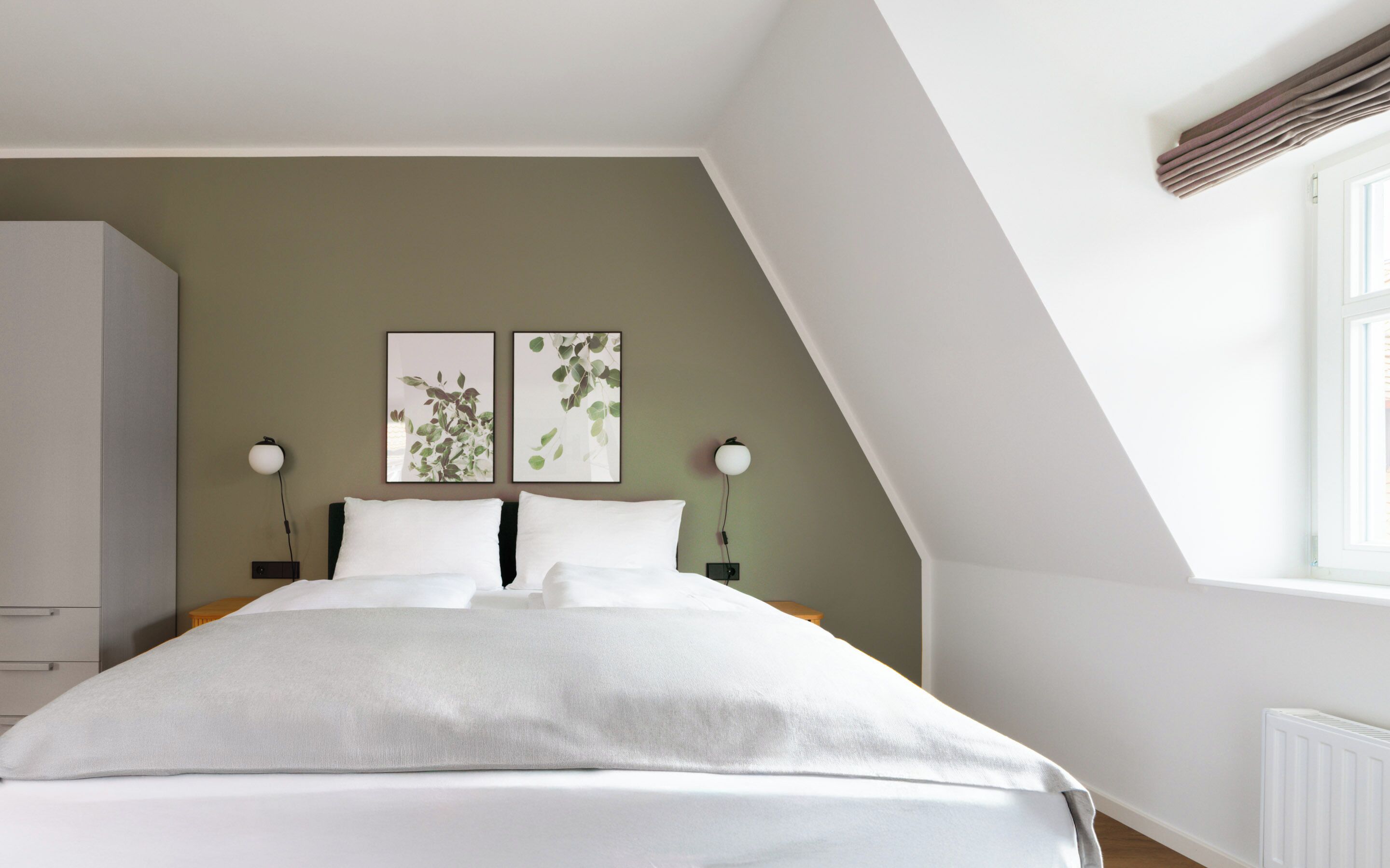 A bedroom with a bed, two bedside tables, a nightstand, a wardrobe, and two wall-mounted lamps.