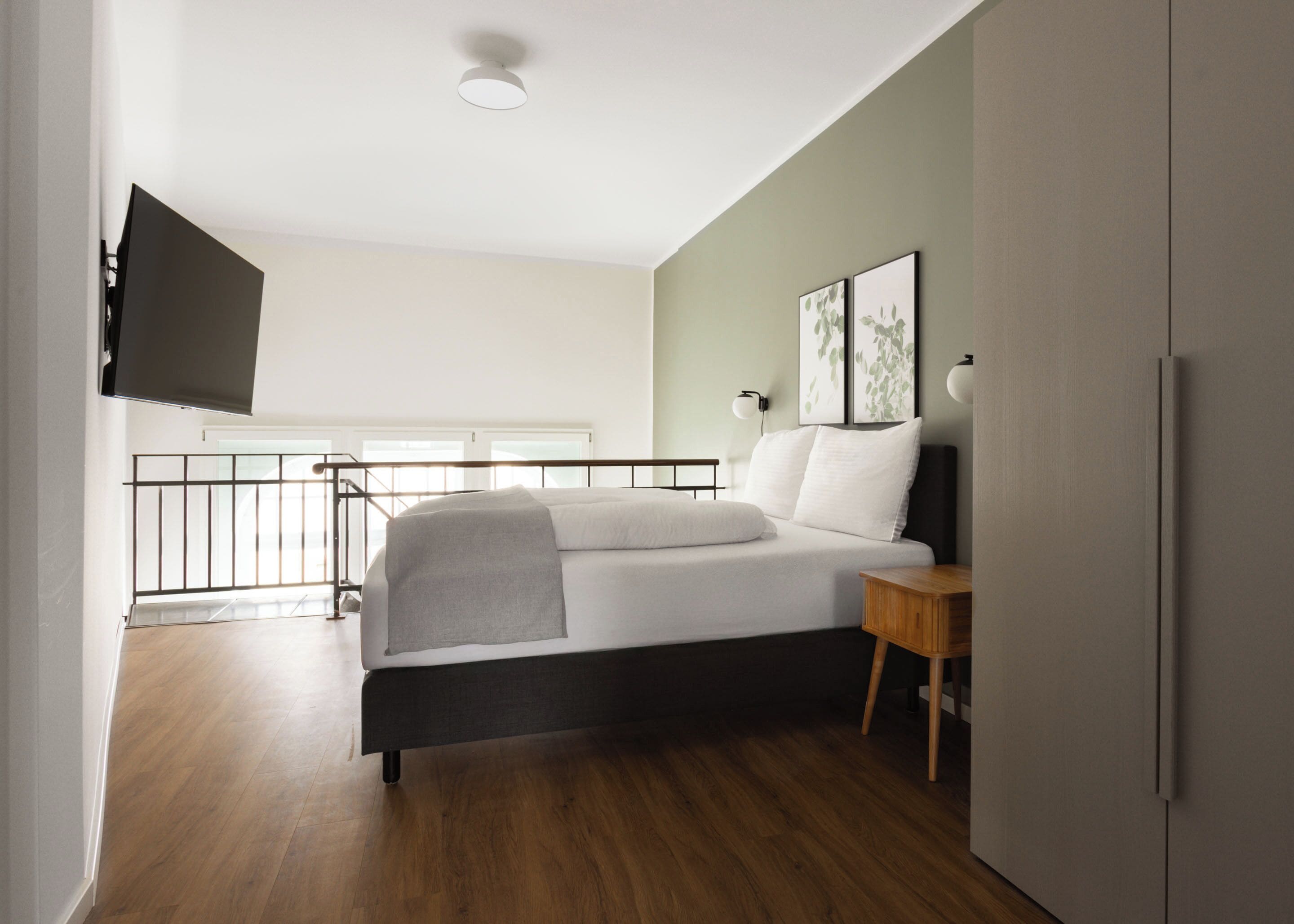 Una camera da letto con un letto, pavimento in legno, una TV montata a parete e una finestra con vista.