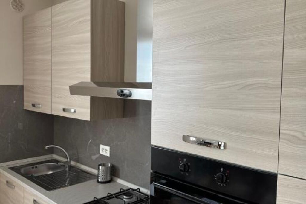 A modern kitchen with light wood cabinetry, a stainless steel sink, and a built-in oven.