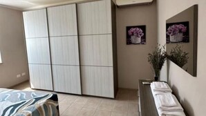 A bedroom with a large wardrobe, a bed with a patterned bedspread, a bedside table with towels, and two framed pictures on the wall. - Tourist Location A Casa di Viola: 1 Bedroom House (Orvieto)