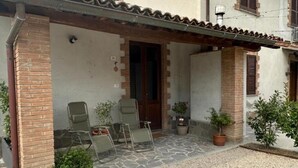 A covered outdoor area with a stone floor, two green chairs, and potted plants. - Tourist Location A Casa di Viola: 1 Bedroom House (Orvieto)