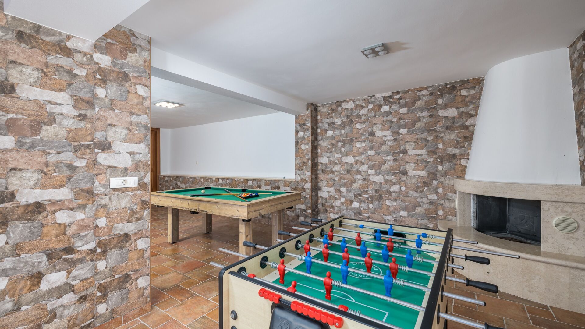 A room with a pool table, foosball table, and a fireplace.