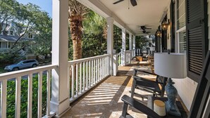 Eine überdachte Veranda mit Deckenventilator, Sitzgelegenheiten im Freien und Blick auf eine Wohnstraße.