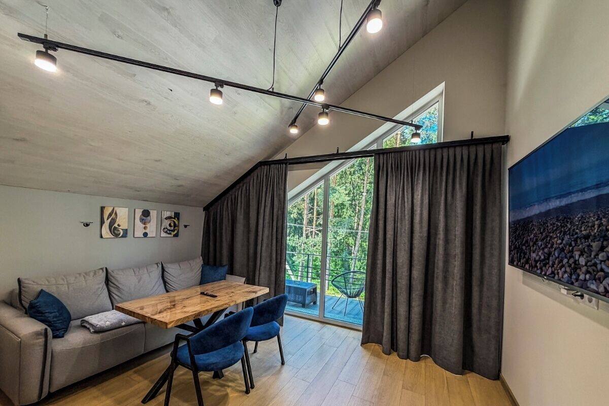 A modern interior with a wooden dining table, blue chairs, a grey sofa, and a large window with curtains.