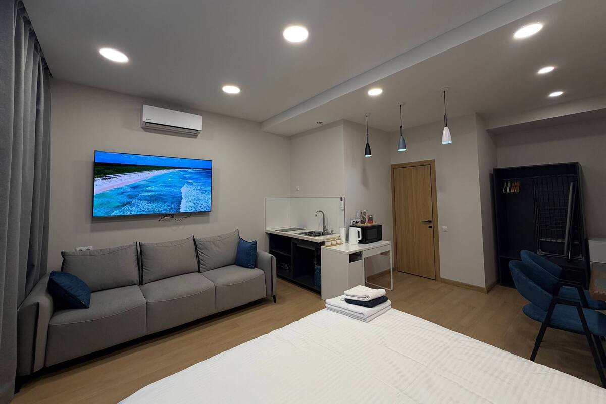 A modern hotel room with a sofa, a bed, a desk, and a television.