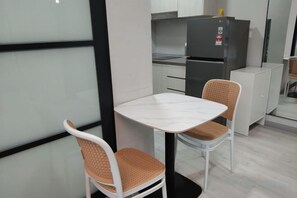 A compact kitchen with a white table and two wicker chairs, a refrigerator, and a white cabinet. - JQ PREMIER SUITES T1 L07 (Kota Kinabalu)