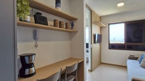 A compact living space with a kitchenette, a dining area, a sofa, and a large window offering a city view. - COFDR0104 - Edifício House Federação (Salvador)
