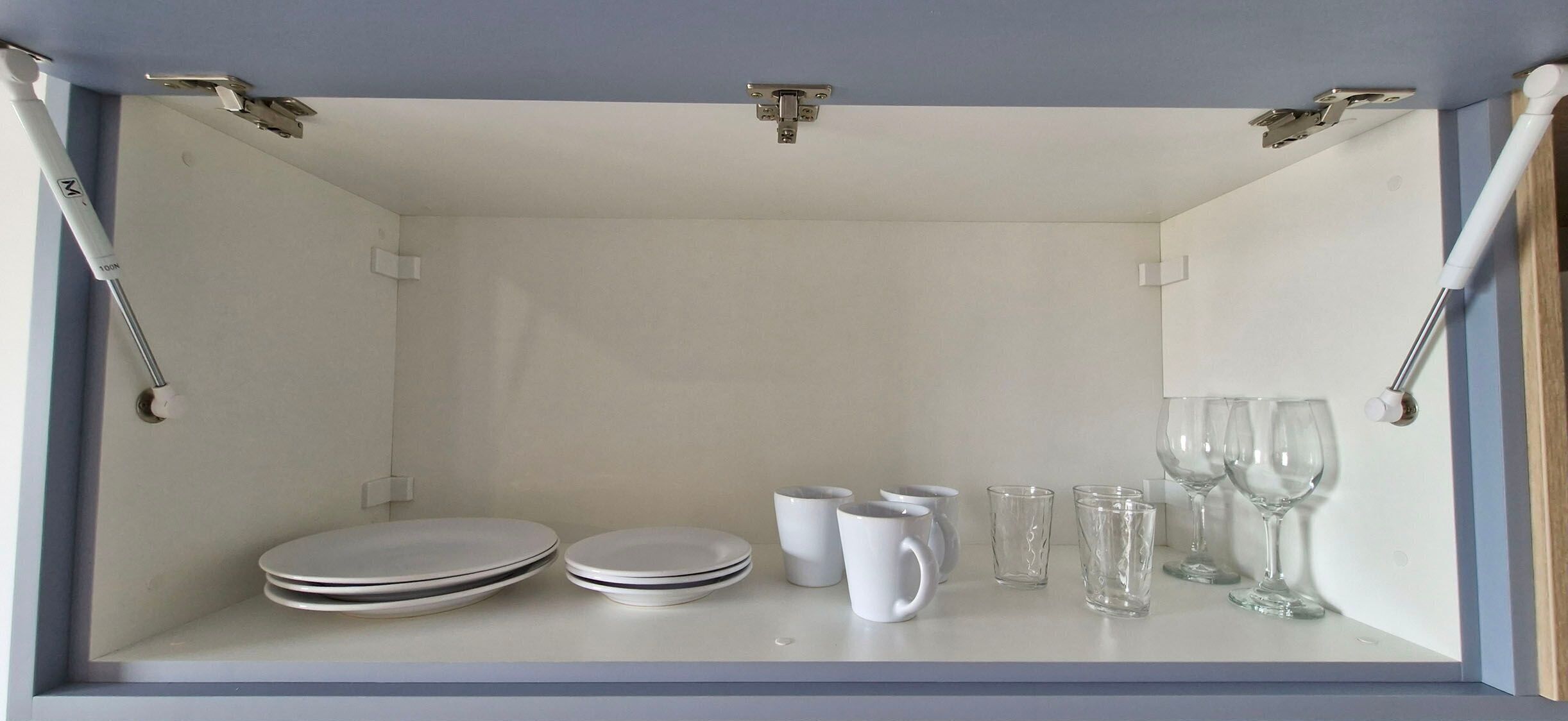 Una habitación con pared y techo blancos, que incluye un estante con platos, tazas y vasos.