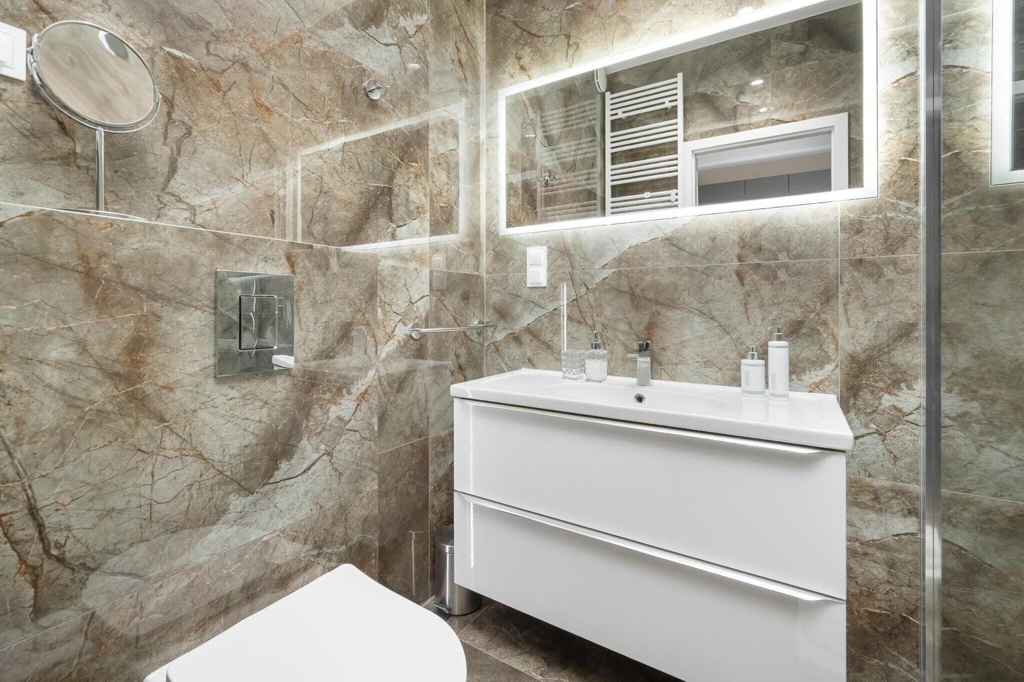 A bathroom with a marble wall, a white vanity, a mirror, and a glass shower enclosure.