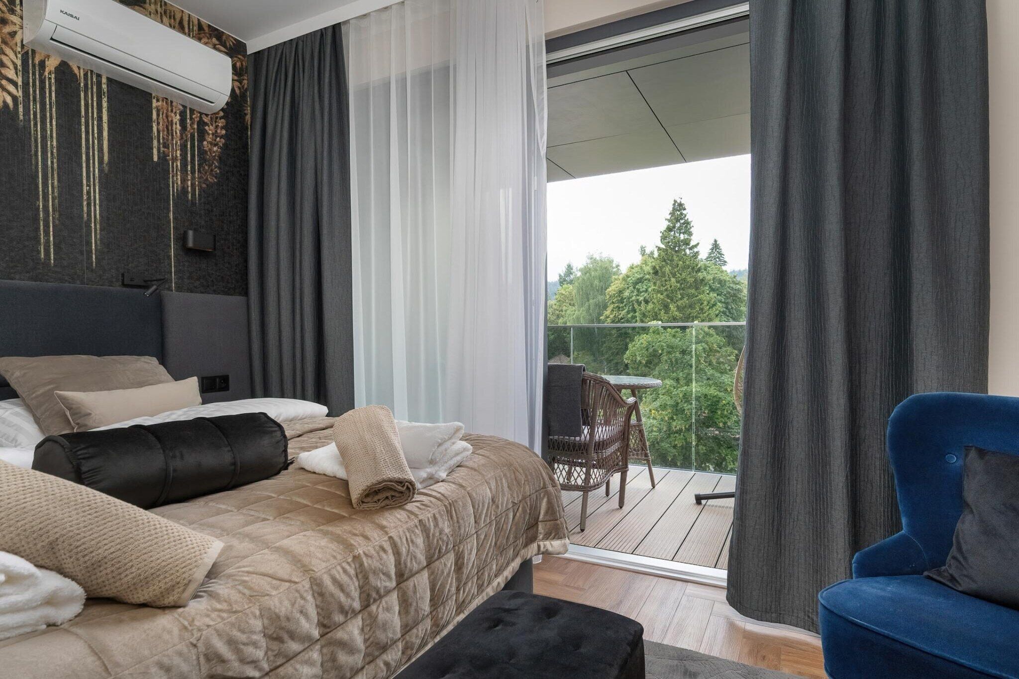A modern bedroom with a large bed, a balcony with a view, and a blue chair.