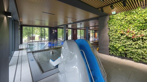 Zona de piscina interior con vista despejada, un tobogán acuático y una pared verde con plantas.