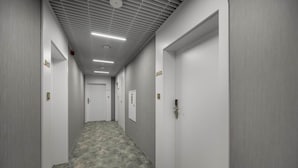 A hallway with doors labeled B411 and B408, a textured carpet, and a ceiling with linear lighting fixtures. - Holiday studio with balcony, indoor pool, sauna (Polanica Zdroj)