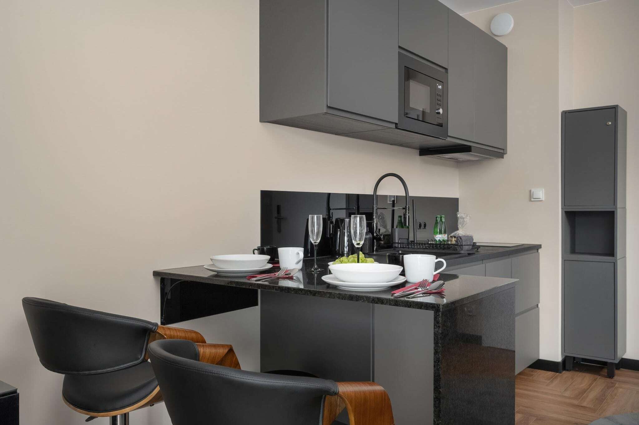 A compact kitchen with a microwave, sink, and a small dining area with chairs and a table set for two.