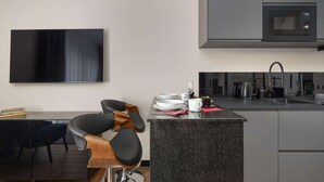 Una cocina moderna con microondas integrado, un comedor con una silla negra y un televisor de pantalla plana montado en la pared.