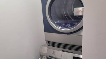 A front view of a washing machine with a front-loading door, a control panel with buttons, and a label instructing to clean the filter after each use.