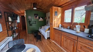 A cozy cabin interior with wooden walls, a green accent wall, a dining area with a table and chairs, a kitchen with wooden cabinets and a sink, and a window with a view of greenery. - CARMEN caravan with SPA (Baron)