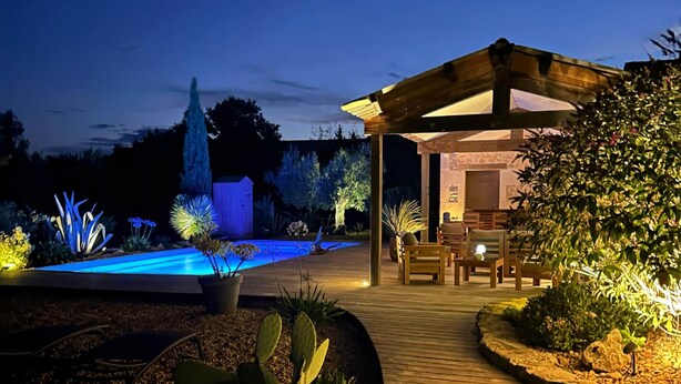 A wooden deck leading to a covered outdoor area with a pool and illuminated plants. - CARMEN caravan with SPA (Baron)