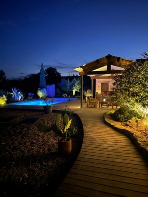A wooden deck leading to a covered outdoor area with a pool and illuminated plants. - CARMEN caravan with SPA (Baron)