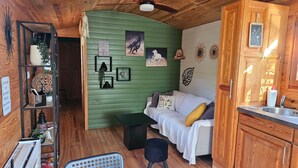 A cozy room with a green wall, a white sofa, a small black table, and a wooden cabinet with a sink. - CARMEN caravan with SPA (Baron)