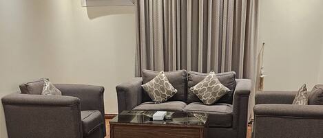 A living room with two grey sofas, a glass coffee table, and a wooden floor.