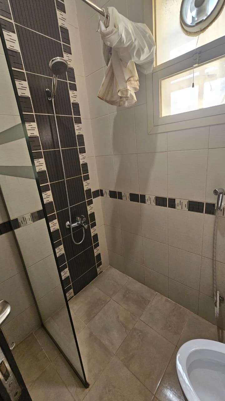 A bathroom with a shower, a toilet, and a window.