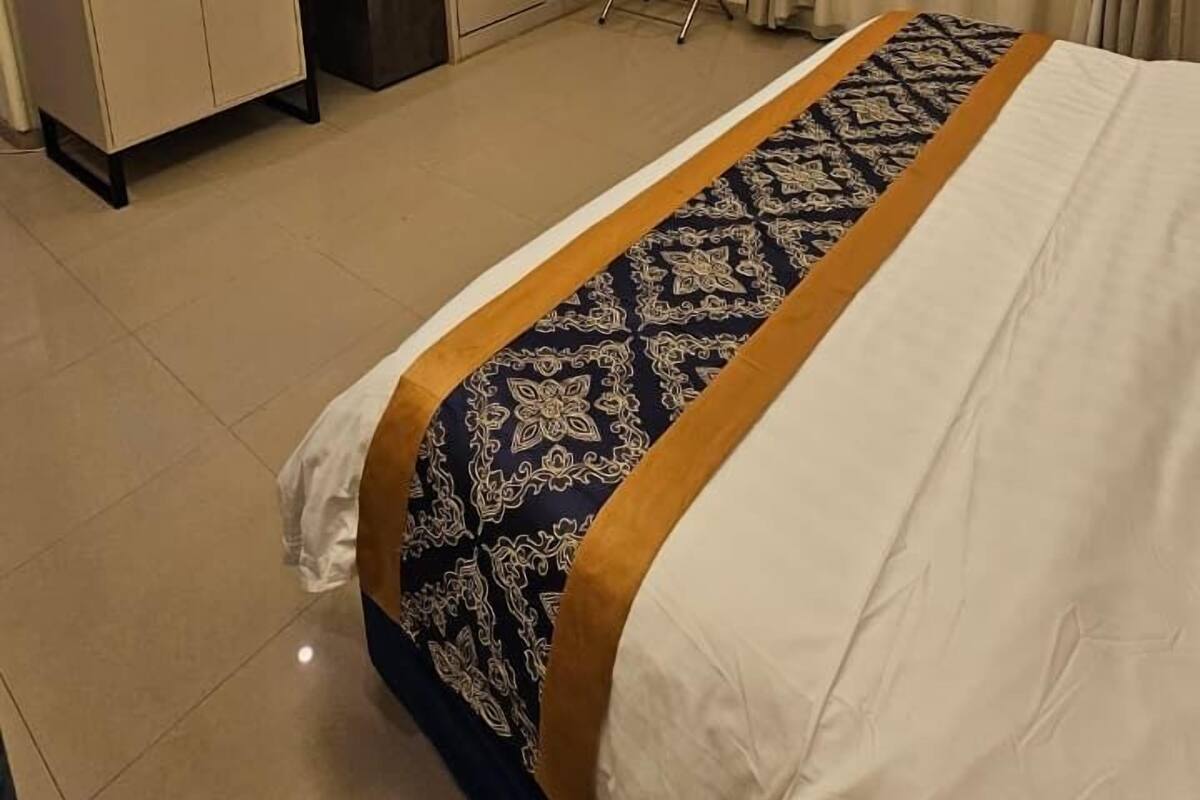 A hotel room with a bed, a desk with a television, a wardrobe, and a chair.